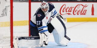 Connor Hellebuyck in Winnipeg Jets gear with Coca-Cola board ad as trade rumors link the Jets goalie to the Sabres and Hurricanes
