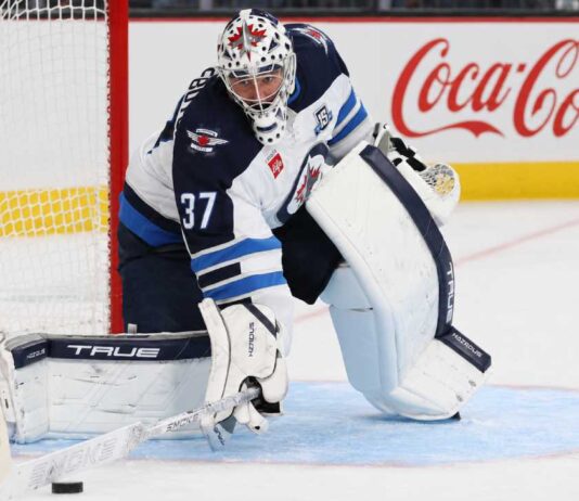 Connor Hellebuyck in Winnipeg Jets gear with Coca-Cola board ad as trade rumors link the Jets goalie to the Sabres and Hurricanes