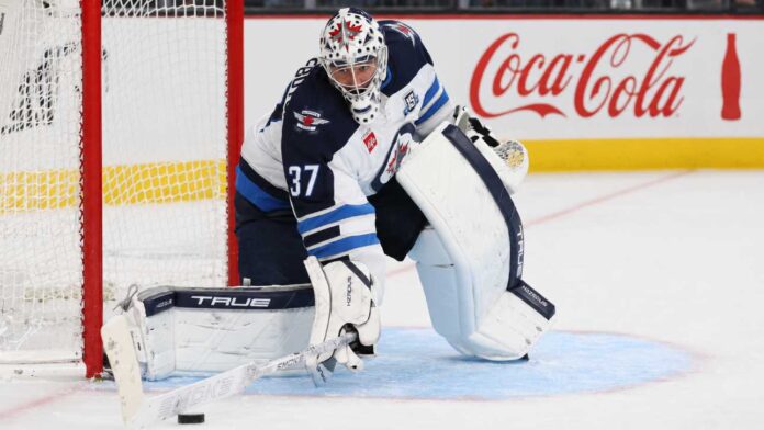 connor-hellebuyck-winnipeg-jets-trade-rumors-skinner-signing Connor Hellebuyck in Winnipeg Jets gear with Coca-Cola board ad as trade rumors link the Jets goalie to the Sabres and Hurricanes