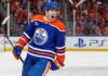 Evan Bouchard Point Projections 2026-27: Edmonton Oilers Forecast Evan Bouchard celebrates in an Edmonton Oilers home jersey beside a PS5 rink-board ad ahead of his 2026-27 fantasy hockey projection