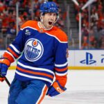 Evan Bouchard Point Projections 2026-27: Edmonton Oilers Forecast Evan Bouchard celebrates in an Edmonton Oilers home jersey beside a PS5 rink-board ad ahead of his 2026-27 fantasy hockey projection