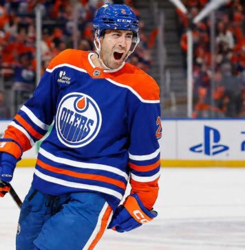 Evan Bouchard Point Projections 2026-27: Edmonton Oilers Forecast Evan Bouchard celebrates in an Edmonton Oilers home jersey beside a PS5 rink-board ad ahead of his 2026-27 fantasy hockey projection