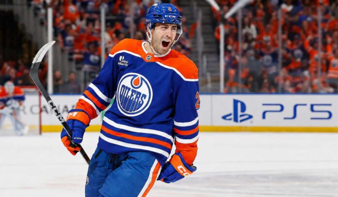 evan-bouchard-oilers-fantasy-projection-2026-27 Evan Bouchard celebrates in an Edmonton Oilers home jersey beside a PS5 rink-board ad ahead of his 2026-27 fantasy hockey projection