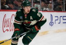 Kirill Kaprizov Fantasy Hockey Projection: Is 100 Points Next? Kirill Kaprizov skating in a Minnesota Wild home jersey beside Coca-Cola and PS5 rink-board ads for a 2026-27 Fantasy Hockey projection
