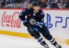 Kyle Connor Fantasy Hockey Projection: Can the Winnipeg Jets Star Reach 100 Points? Kyle Connor skating in a Winnipeg Jets home jersey beside Coca-Cola and PS5 board ads for a 2026-27 Fantasy Hockey projection.