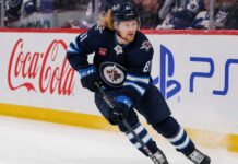 Kyle Connor skating in a Winnipeg Jets home jersey beside Coca-Cola and PS5 board ads for a 2026-27 Fantasy Hockey projection.