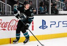 Macklin Celebrini Point Projections 2026-27: San Jose Sharks Fantasy Hockey Outlook Macklin Celebrini skating for the San Jose Sharks with Coca-Cola and PS5 board ads, highlighting his 2026-27 fantasy hockey point projection