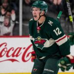 Matt Boldy Point Projections 2026-27: Minnesota Wild Fantasy Outlook Matt Boldy celebrating in a Minnesota Wild jersey beside a Coca-Cola board ad for his 2026-27 fantasy hockey point projection.