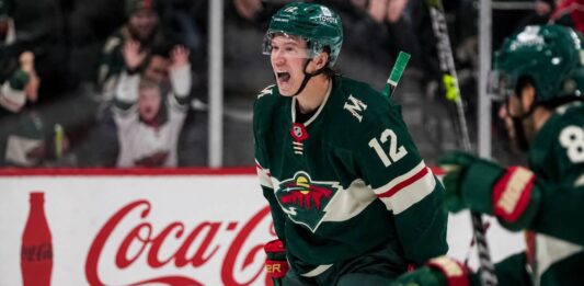 Matt Boldy Point Projections 2026-27: Minnesota Wild Fantasy Outlook Matt Boldy celebrating in a Minnesota Wild jersey beside a Coca-Cola board ad for his 2026-27 fantasy hockey point projection.