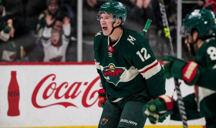 matt-boldy-minnesota-wild-fantasy-hockey-projection-2026-27 Matt Boldy celebrating in a Minnesota Wild jersey beside a Coca-Cola board ad for his 2026-27 fantasy hockey point projection.