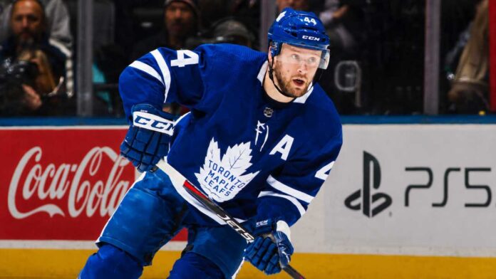 morgan-rielly-maple-leafs-trade-rumors-2026 Morgan Rielly skating in a Toronto Maple Leafs home jersey as trade rumors suggest the veteran defenseman could remain in Toronto for the 2026-27 NHL season.