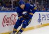 Tage Thompson Point Projections 2026-27: Buffalo Sabres Fantasy Hockey Outlook Tage Thompson skating right-handed along the boards in a Buffalo Sabres jersey beside Coca-Cola and PS5 ads during an NHL game.