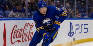 Tage Thompson Point Projections 2026-27: Buffalo Sabres Fantasy Hockey Outlook Tage Thompson skating right-handed along the boards in a Buffalo Sabres jersey beside Coca-Cola and PS5 ads during an NHL game.