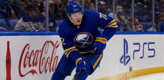 Tage Thompson Point Projections 2026-27: Buffalo Sabres Fantasy Hockey Outlook Tage Thompson skating right-handed along the boards in a Buffalo Sabres jersey beside Coca-Cola and PS5 ads during an NHL game.