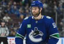Shane Wright wearing a Vancouver Canucks home jersey amid trade rumors involving the Seattle Kraken, Zeev Buium and Tom Willander.