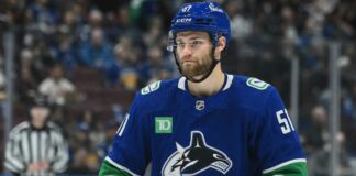 Shane Wright wearing a Vancouver Canucks home jersey amid trade rumors involving the Seattle Kraken, Zeev Buium and Tom Willander.