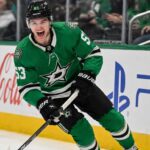 Wyatt Johnston Point Projections 2026-27: Can the Dallas Stars Star Reach 90 Points Again? Wyatt Johnston skating in a Dallas Stars home jersey beside Coca-Cola and PS5 ads for his 2026-27 fantasy hockey point projection.