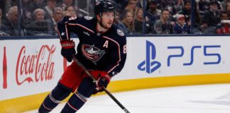 Zach Werenski Point Projections 2026-27: Columbus Blue Jackets Fantasy Outlook Zach Werenski skating left-handed for the Columbus Blue Jackets beside Coca-Cola and PS5 board ads during a 2026-27 fantasy hockey projection