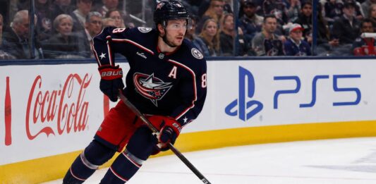 Zach Werenski Point Projections 2026-27: Columbus Blue Jackets Fantasy Outlook Zach Werenski skating left-handed for the Columbus Blue Jackets beside Coca-Cola and PS5 board ads during a 2026-27 fantasy hockey projection