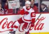 Alex DeBrincat Trade Rumors: Could the Detroit Red Wings Move Another Star? Alex DeBrincat celebrates for the Detroit Red Wings as a fan holds a “Please stay in Detroit Alex!” sign amid NHL trade rumors.