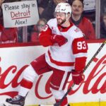 Alex DeBrincat Trade Rumors: Could the Detroit Red Wings Move Another Star? Alex DeBrincat celebrates for the Detroit Red Wings as a fan holds a “Please stay in Detroit Alex!” sign amid NHL trade rumors.