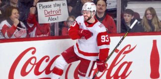 Alex DeBrincat Trade Rumors: Could the Detroit Red Wings Move Another Star? Alex DeBrincat celebrates for the Detroit Red Wings as a fan holds a “Please stay in Detroit Alex!” sign amid NHL trade rumors.