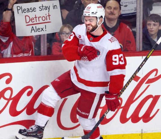 Alex DeBrincat Trade Rumors: Could the Detroit Red Wings Move Another Star? Alex DeBrincat celebrates for the Detroit Red Wings as a fan holds a “Please stay in Detroit Alex!” sign amid NHL trade rumors.