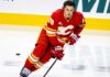 Calgary Flames defenseman Zach Whitecloud skates in a red Flames jersey amid NHL trade rumors linking him to a possible move.