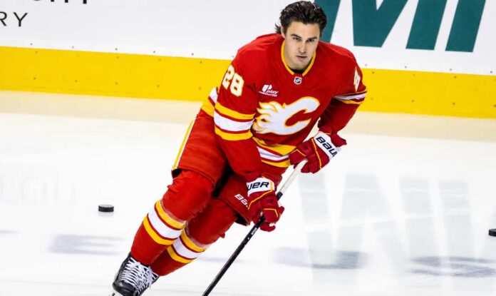 zach-whitecloud-calgary-flames-trade-rumors (1) Calgary Flames defenseman Zach Whitecloud skates in a red Flames jersey amid NHL trade rumors linking him to a possible move.