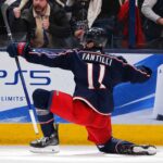 Adam Fantilli Fantasy Hockey Projection 2026-27: Is a 72-Point Breakout Coming? Adam Fantilli of the Columbus Blue Jackets celebrates a goal in front of the crowd as a stylish PS5 rink board ad highlights his 2026-27 fantasy hockey breakout outlook.