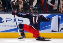 Adam Fantilli Fantasy Hockey Projection 2026-27: Is a 72-Point Breakout Coming? Adam Fantilli of the Columbus Blue Jackets celebrates a goal in front of the crowd as a stylish PS5 rink board ad highlights his 2026-27 fantasy hockey breakout outlook.