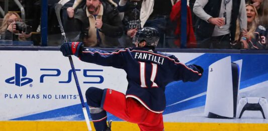 Adam Fantilli of the Columbus Blue Jackets celebrates a goal in front of the crowd as a stylish PS5 rink board ad highlights his 2026-27 fantasy hockey breakout outlook.