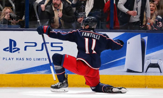 adam-fantilli-columbus-blue-jackets-fantasy-hockey-2026-27 Adam Fantilli of the Columbus Blue Jackets celebrates a goal in front of the crowd as a stylish PS5 rink board ad highlights his 2026-27 fantasy hockey breakout outlook.
