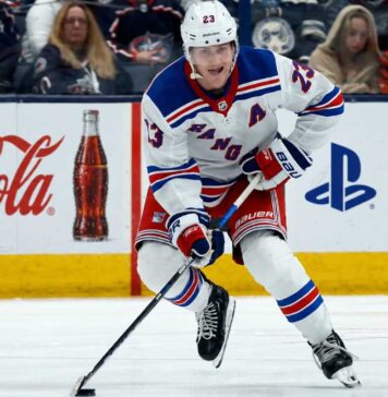Adam Fox Point Projections 2026-27: New York Rangers Fantasy Outlook Adam Fox skating for the New York Rangers beside Coca-Cola and PS5 board ads in a 2026-27 fantasy hockey point projection.