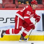 Alex DeBrincat Trade Rumors: Could Detroit’s Front-Office Chaos Put Another 40-Goal Star in Play? Detroit Red Wings forward in a home red jersey skating with the puck in a concept image for Alex DeBrincat trade rumors and Detroit Red Wings front-office uncertainty.