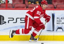 Alex DeBrincat Trade Rumors: Could Detroit’s Front-Office Chaos Put Another 40-Goal Star in Play? Detroit Red Wings forward in a home red jersey skating with the puck in a concept image for Alex DeBrincat trade rumors and Detroit Red Wings front-office uncertainty.