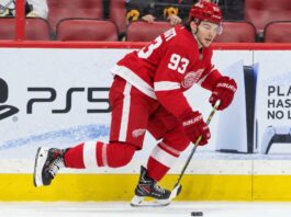 Alex DeBrincat Trade Rumors: Could Detroit’s Front-Office Chaos Put Another 40-Goal Star in Play? Detroit Red Wings forward in a home red jersey skating with the puck in a concept image for Alex DeBrincat trade rumors and Detroit Red Wings front-office uncertainty.
