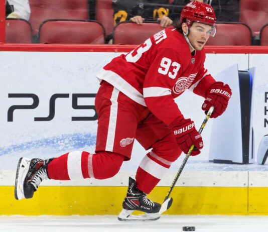 Alex DeBrincat Trade Rumors: Could Detroit’s Front-Office Chaos Put Another 40-Goal Star in Play? Detroit Red Wings forward in a home red jersey skating with the puck in a concept image for Alex DeBrincat trade rumors and Detroit Red Wings front-office uncertainty.