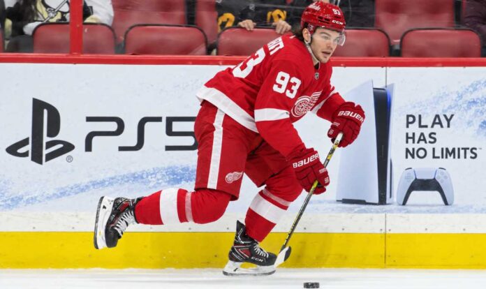 alex-debrincat-detroit-red-wings-trade-rumors-image Detroit Red Wings forward in a home red jersey skating with the puck in a concept image for Alex DeBrincat trade rumors and Detroit Red Wings front-office uncertainty.