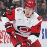 Alexander Nikishin Trade Rumors: Did His Hurricanes Camp Absence Just Force Carolina’s Hand? Alexander Nikishin of the Carolina Hurricanes skates with the puck during game action with Coca-Cola and Samsung ads on the boards in the background