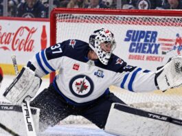 Connor Hellebuyck makes a glove save for the Winnipeg Jets as NHL trade rumors intensify ahead of training camp.