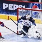Nick Suzuki of the Montreal Canadiens attacks the net against Winnipeg Jets goalie Connor Hellebuyck amid NHL trade rumors linking Hellebuyck to Montreal.