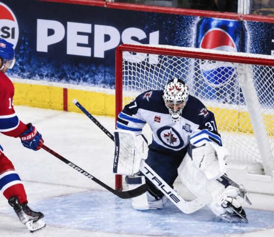 Nick Suzuki of the Montreal Canadiens attacks the net against Winnipeg Jets goalie Connor Hellebuyck amid NHL trade rumors linking Hellebuyck to Montreal.