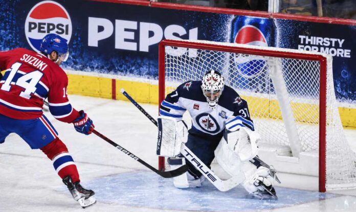 Nick Suzuki of the Montreal Canadiens attacks the net against Winnipeg Jets goalie Connor Hellebuyck amid NHL trade rumors linking Hellebuyck to Montreal.