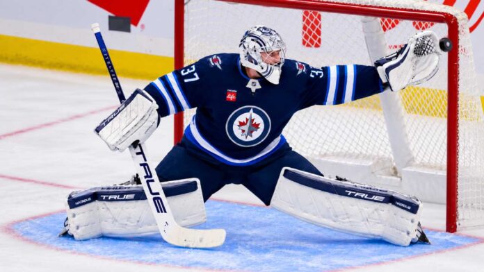 connor-hellebuyck-st-louis-blues-hurricanes-trade-rumors Connor Hellebuyck of the Winnipeg Jets makes a save amid trade rumors involving the Carolina Hurricanes and St. Louis Blues.