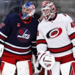 Connor Hellebuyck of the Winnipeg Jets talks with a Carolina Hurricanes goalie during NHL trade rumor speculation linking Hellebuyck to Carolina