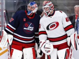 Connor Hellebuyck of the Winnipeg Jets talks with a Carolina Hurricanes goalie during NHL trade rumor speculation linking Hellebuyck to Carolina