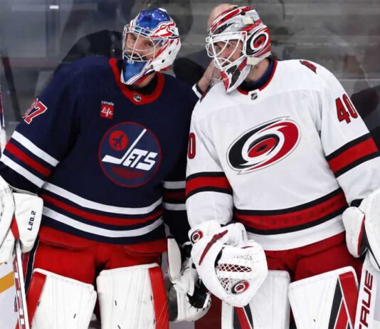 Connor Hellebuyck of the Winnipeg Jets talks with a Carolina Hurricanes goalie during NHL trade rumor speculation linking Hellebuyck to Carolina