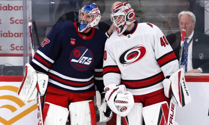 connor-hellebuyck-trade-rumors-carolina-hurricanes-nikishin Connor Hellebuyck of the Winnipeg Jets talks with a Carolina Hurricanes goalie during NHL trade rumor speculation linking Hellebuyck to Carolina