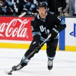 Dylan Guenther Point Projections 2026-27: Utah Mammoth Fantasy Outlook Dylan Guenther skating for the Utah Mammoth beside Coca-Cola and PS5 board ads in a 2026-27 fantasy hockey point projection.